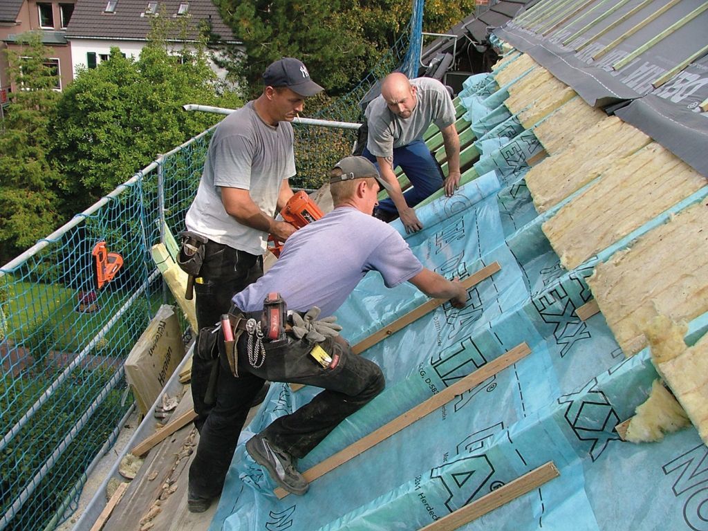Drei Arbeiter dämmen ein Steildach mit Dachfolie