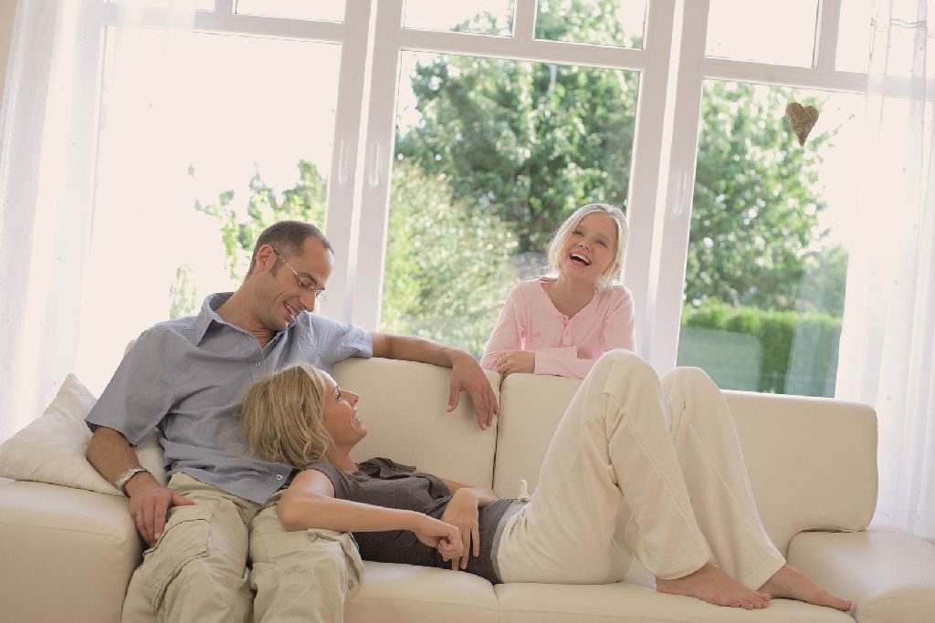 glückliche Familie auf dem Sofa, im Hintergrund große Fensterflächen