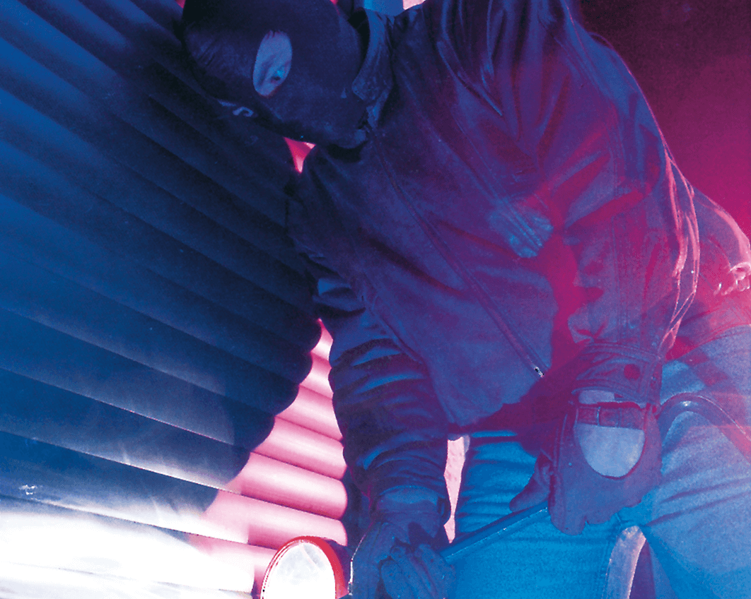 Einbrecher mit Sturmmaske und Taschenlampe versucht mit einem Kuhfuss einbruchhemmende Rollläden aufzuhebeln.