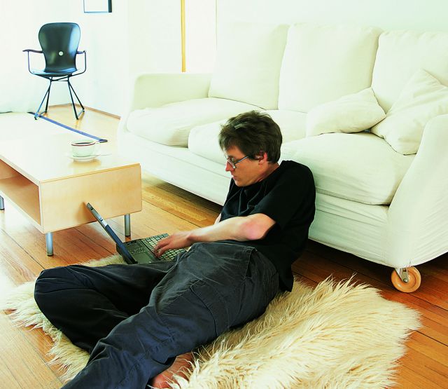 Trotz Altbauten: Ein Mann liegt entspannt und barfuß auf einem Teppich im Wohnzimmer und benutzt einen Laptop