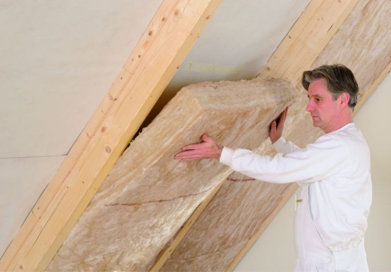 Ein Facharbeiter dämmt die Wände eines Dachbodens mit Mineralwolle