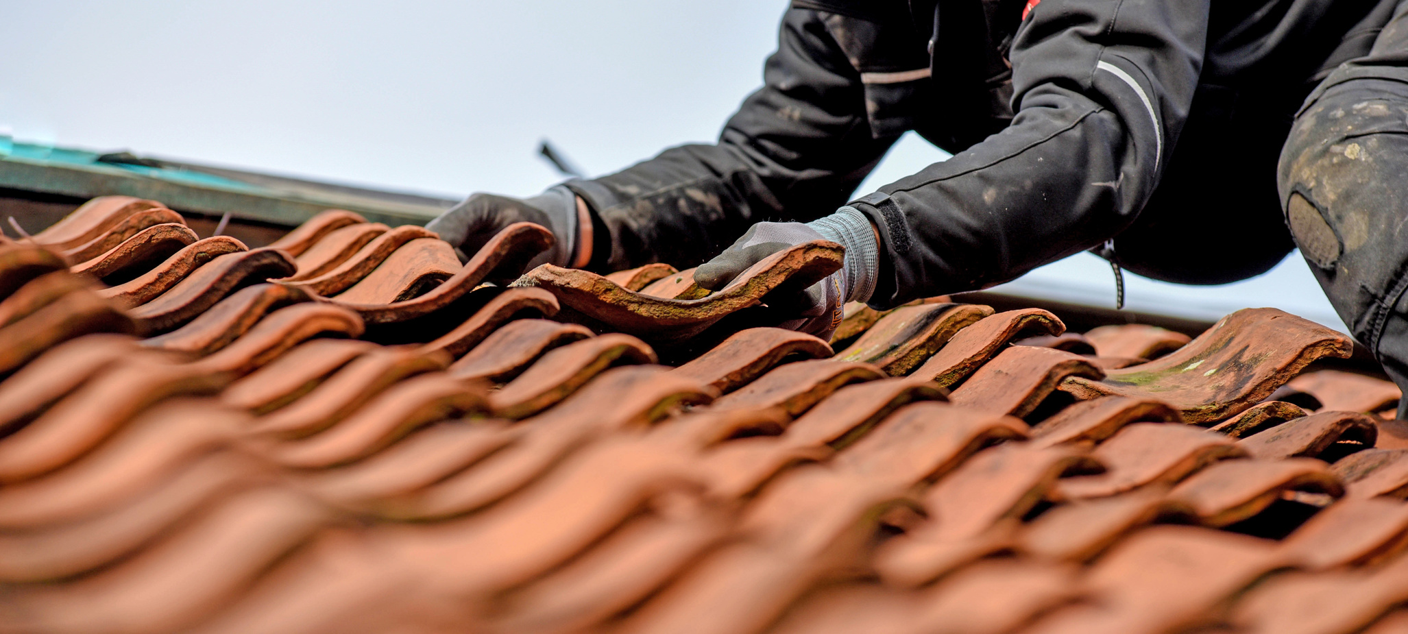 Ein Handwerker entfernt einen defekten Dachziegel.