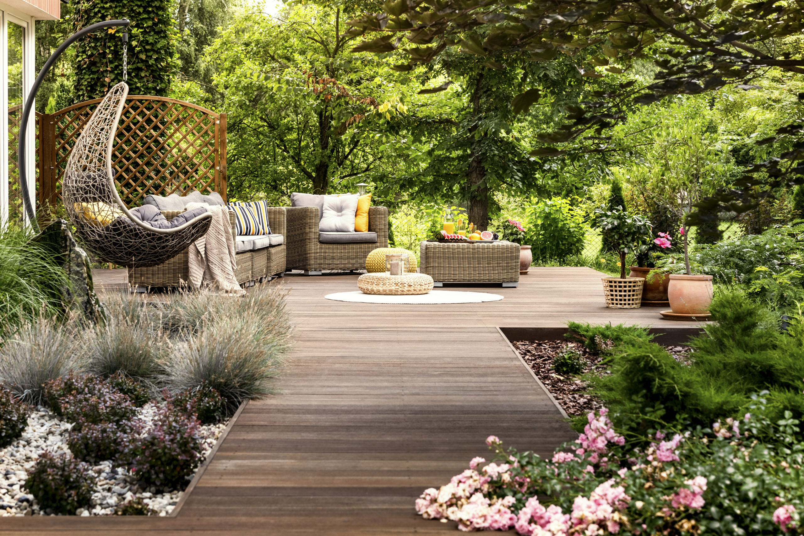 Ökologisch bauen: eine Terrasse aus Holz, umgeben von vielen bunten Blumen und grünen Bäumen.