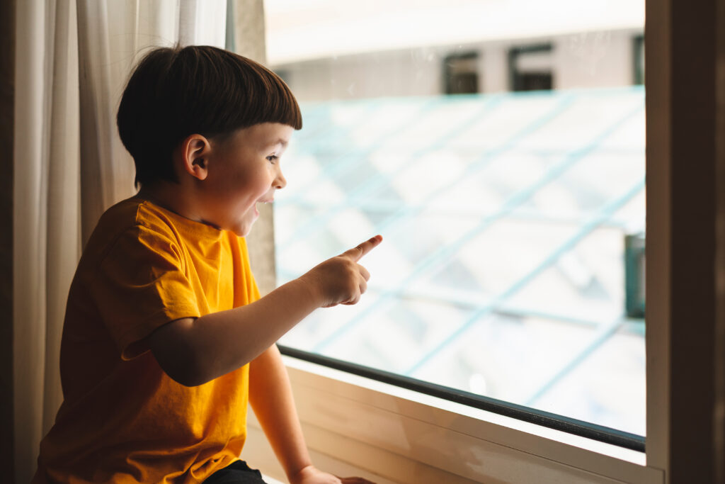 Kleiner Junge schaut aus dem Fenster und zeigt mit dem Finger an die Scheibe. 