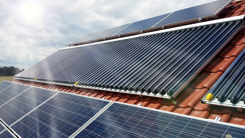 Solarthermie-Röhrenkollektoren und Photovoltaik-Module auf einem Ziegeldach bei Sonnenschein